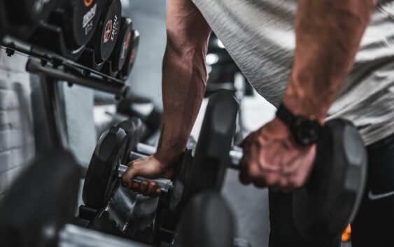 person in gray shirt holding black dumbbell